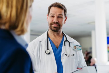 Kadın tıbbi satış temsilcisi. Doktora ilaç sunuyor. Hastane koridorunda duruyor..