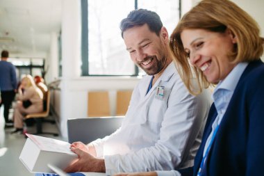 İlaç mümessili ve doktor ilaç örnekleri ve reçeteleri tartışıyor, hastane bekleme odasında oturuyor..