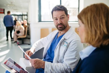İlaç mümessili ve doktor ilaç örnekleri ve reçeteleri tartışıyor, hastane bekleme odasında oturuyor..