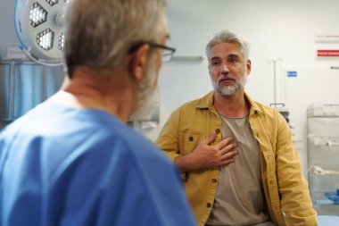 Muayene masasında oturan hasta, doktorlara sağlık sorunları ve semptomları anlatıyor..