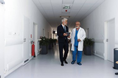 Doktor hastane müdürüyle konuşuyor, hastane koridorunda yürüyor..