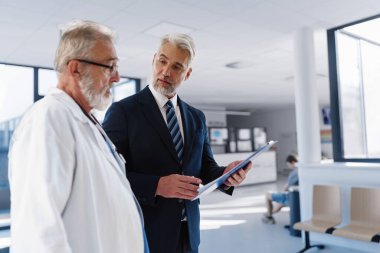 Doktor hastane müdürüyle konuşuyor, hastane koridorunda yürüyor..