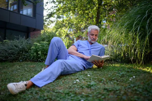 Sağlık çalışanı hastanenin dışındaki parkta dinleniyor ve tatilde kitap okuyor..