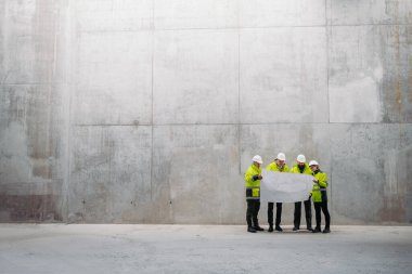 Mühendisler ve inşaat işçileri modern inşaat alanının planlarını inceliyor..