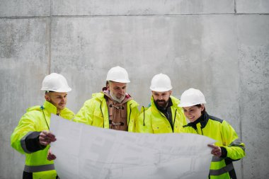 Mühendisler ve inşaat işçileri modern inşaat alanının planlarını inceliyor..