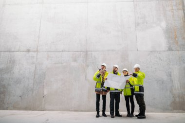 Mühendisler ve inşaat işçileri modern inşaat alanının planlarını inceliyor..