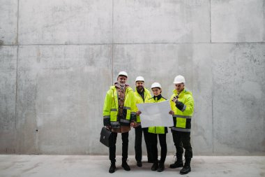 Mühendisler ve inşaat işçileri modern inşaat alanının planlarını inceliyor..