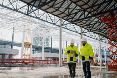 İnşaat yöneticileri mekanda dijital tablet kullanıyor, proje planlarını içeride gözden geçiriyorlar.