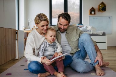 Ebeveynler küçük oğluyla kitap okuyor, yerde oturuyor. Bağlanma anı.