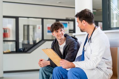 Genç çocuk gülümsüyor yardımcı doktorla konuşuyor, olumlu sağlık haberleri alıyor..