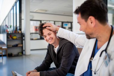 Genç çocuk gülümsüyor yardımcı doktorla konuşuyor, olumlu sağlık haberleri alıyor..