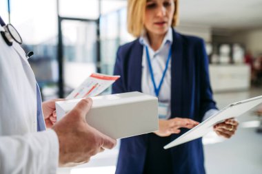 Kadın tıbbi satış temsilcisi. Doktora ilaç sunuyor. Hastane koridorunda duruyor..