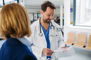 Kadın tıbbi satış temsilcisi. Doktora ilaç sunuyor. Hastane koridorunda duruyor..