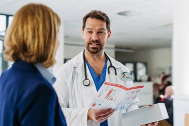 Kadın tıbbi satış temsilcisi. Doktora ilaç sunuyor. Hastane koridorunda duruyor..