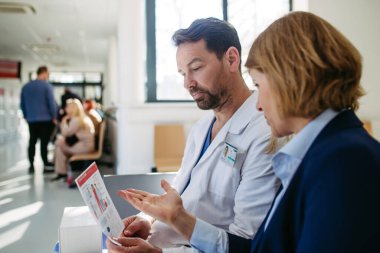 İlaç mümessili ve doktor ilaç örnekleri ve reçeteleri tartışıyor, hastane bekleme odasında oturuyor..