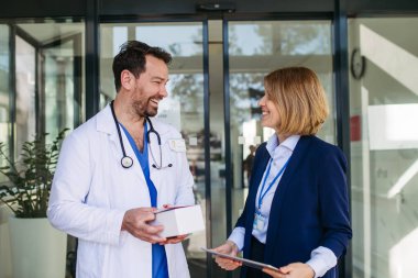 Kadın tıbbi satış temsilcisi. Doktora ilaç sunuyor. Hastane koridorunda duruyor..