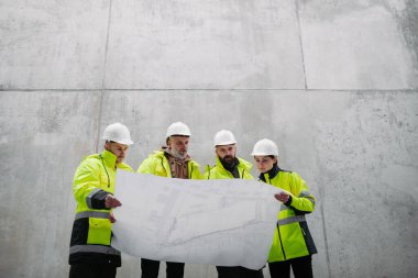 Mühendisler ve inşaat işçileri modern inşaat alanının planlarını inceliyor..