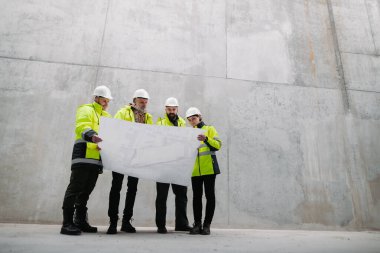 Mühendisler ve inşaat işçileri modern inşaat alanının planlarını inceliyor..