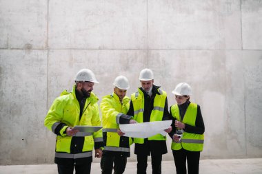 Mühendisler ve inşaat işçileri modern inşaat alanının planlarını inceliyor..