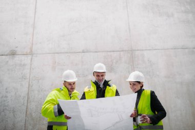 Mühendisler ve inşaat işçileri modern inşaat alanının planlarını inceliyor..