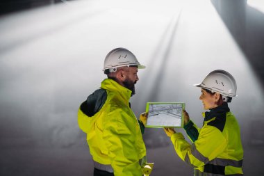 Mühendisler modern inşaat alanında bir tablet kullanarak inşaat planlarını tartışıyorlar.