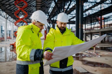 İnşaat yöneticileri modern inşaat alanındaki proje planlarını gözden geçiriyorlar.