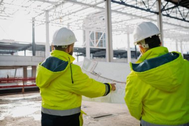 İnşaat yöneticileri modern inşaat alanındaki proje planlarını gözden geçiriyorlar.