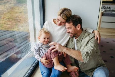Ebeveynler küçük oğluyla oynuyorlar, pencerenin kenarında oturuyorlar. Bağlanma anı.