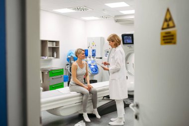 Doktorun tomografi sonucunu paylaşması görüntüleme odasında gülümseyen bir hastayla, tıbbi tedavi....