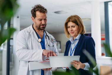 Kadın tıbbi satış temsilcisi. Doktora ilaç sunuyor. Hastane koridorunda duruyor..