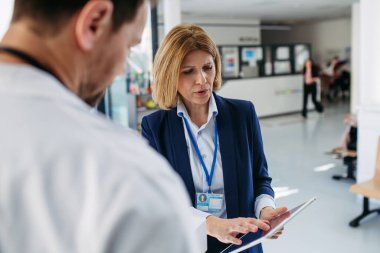 Kadın tıbbi satış temsilcisi. Doktora ilaç sunuyor. Hastane koridorunda duruyor..