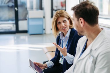 İlaç mümessili ve doktor yeni ilaç ve reçeteleri açıklıyor, hastanede bekleme odasında oturuyor..
