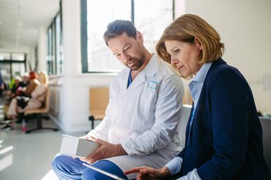 İlaç mümessili ve doktor yeni ilaç ve reçeteleri açıklıyor, hastanede bekleme odasında oturuyor..