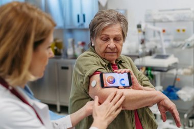 Endokrinolog, yaşlı hastaya sürekli glikoz monitörünü mobil uygulamayla nasıl bağlayacağını öğretiyor. Kıdemli sağlık hizmetleri.