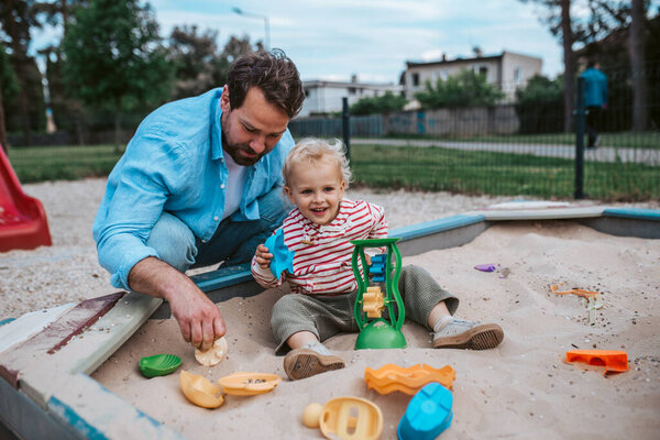 Отец и младший сын играют в песочнице на детской площадке, веселье на выходных.