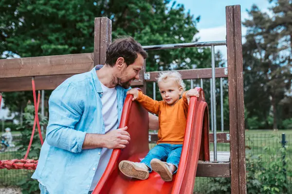Babalarının desteğiyle kaydırağın üzerinde yürüyordu. Baba ve oğul oyun alanında eğleniyor..