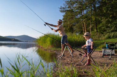Baba ve küçük oğlu göl kıyısında birlikte balık tutuyor. Babalar Günü konsepti.