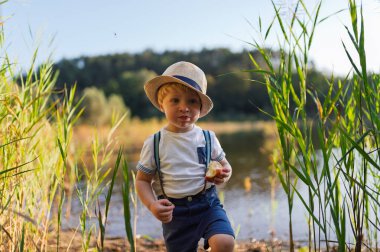 Lastik botlarla gölün sığ sularında yürüyen bir çocuk. Boşluğu kopyala.