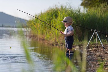 Göl kıyısında balık tutan küçük çocuğun yan görüntüsü. Boşluğu kopyala.