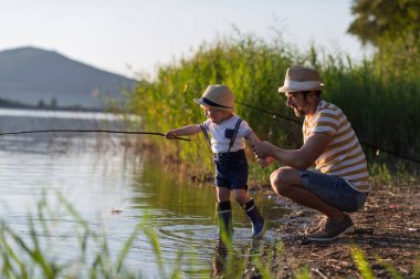 Babası küçük oğluna gölde balık tutmayı öğretiyor.