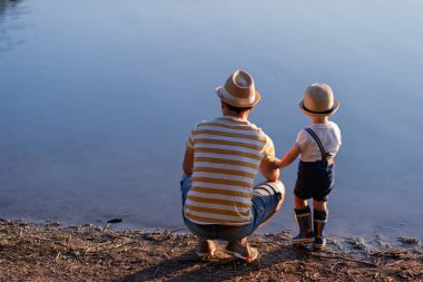 Baba ve küçük oğlu gölde suya bakıyor, doğada huzurlu bir anın tadını çıkarıyorlar..