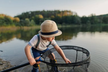 Çocuk gölün kenarında balık ağıyla oynuyor, doğada kaygısız bir anın tadını çıkarıyor..
