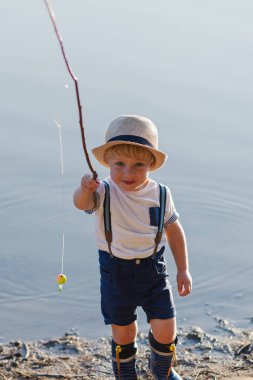 Günbatımında bir gölün yanında bekleyen bir şapka ile bir küçük yürümeye başlayan çocuk. Kopya alanı.