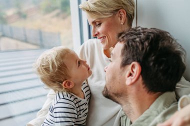 Ebeveynler küçük oğluyla oynuyorlar, pencerenin kenarında oturuyorlar. Bağlanma anı.