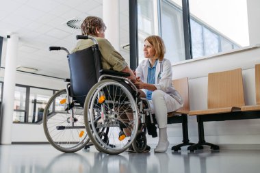 Tekerlekli sandalyedeki yaşlı hasta kadın doktorla konuşuyor. Kıdemli sağlık hizmetleri.