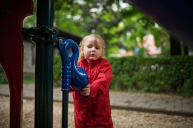 Kırmızı yağmurluklu çocuk şehirde boş zaman geçiriyor..
