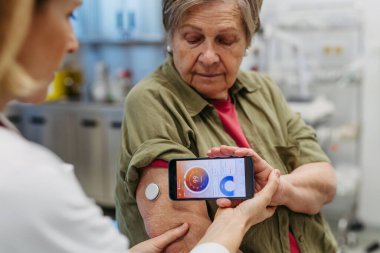 Endokrinolog, yaşlı hastaya sürekli glikoz monitörünü mobil uygulamayla nasıl bağlayacağını öğretiyor. Kıdemli sağlık hizmetleri.