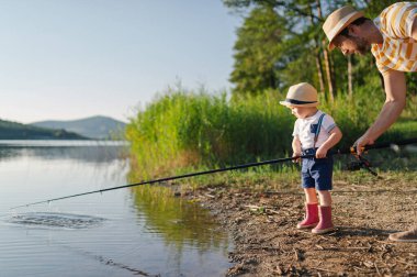 Babası küçük oğluna gölde balık tutmayı öğretiyor.