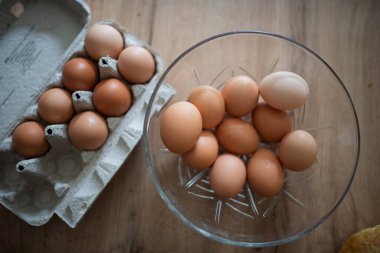 Karton ve cam kasede taze kahverengi yumurtalar. Ahşap mutfak masasında taze çiftlik yumurtaları.