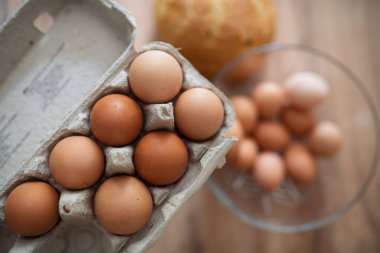 Karton ve cam kasede taze kahverengi yumurtalar. Ahşap mutfak masasında taze çiftlik yumurtaları.